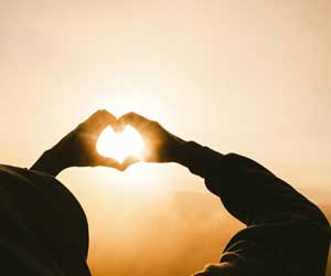 Hands giving a heart sign up to the sun