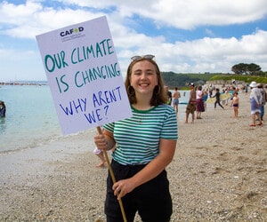 CAFOD climate campaigner holding up placard at the beach